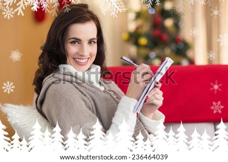 Brunette lying on the couch writing her christmas list against fir tree forest and snowflakes