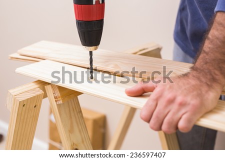 Casual man drilling hole in plank at home in the living room