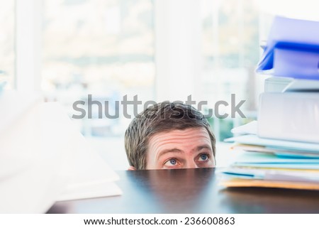 Scared businessman peeking over desk in his office