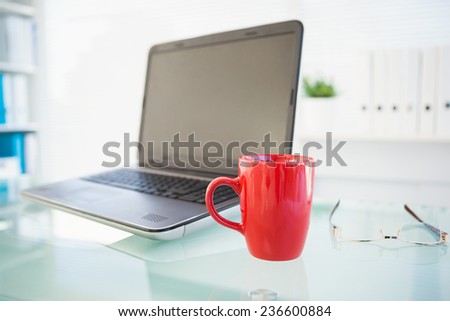 Laptop on desk with red mug and glasses in the office