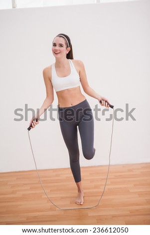 Fit brunette using skipping rope on wooden floor