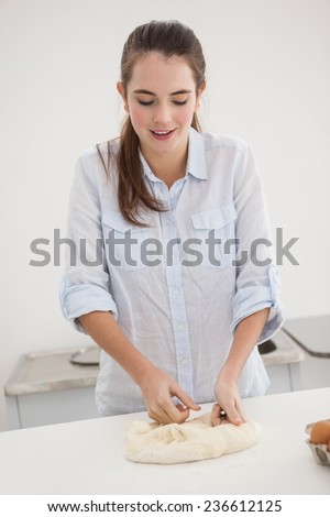 Pretty brunette kneading dough on counter at home in the kitchen
