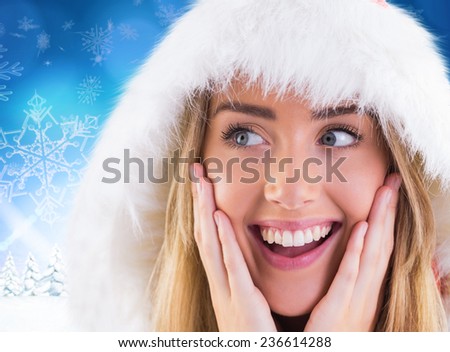 Pretty santa girl with hands on face against snowy landscape with fir trees