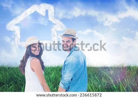 Happy hipster couple holding hands and smiling at camera against field of grass under blue sky