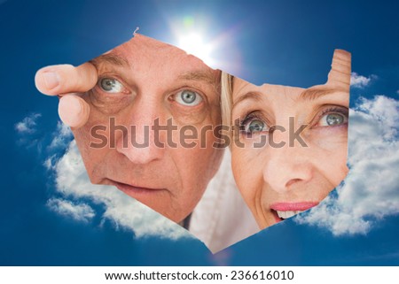 Older couple looking through rip against blue sky with clouds and sun
