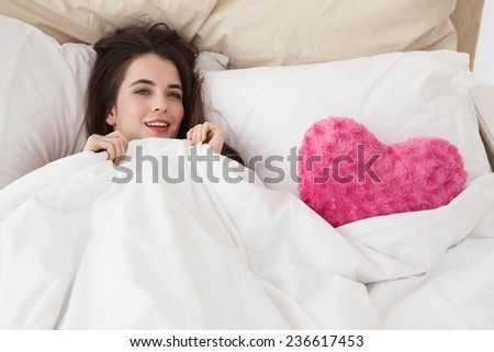 Pretty brunette in bed with heart cushion at home in the bedroom