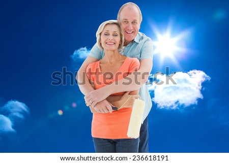 Happy older couple holding paint roller against bright blue sky with clouds
