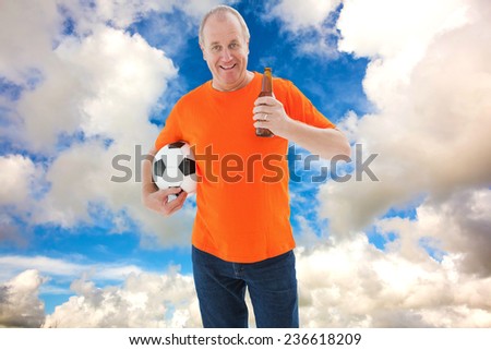 Mature man in orange tshirt holding football and beer against blue sky with white clouds