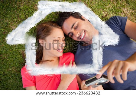 Two smiling friends looking at photos on a camera against house outline in clouds