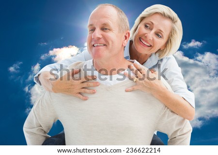 Happy mature man giving piggy back to partner against blue sky with clouds and sun