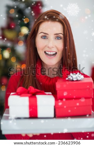 Festive redhead holding pile of gifts against snow falling