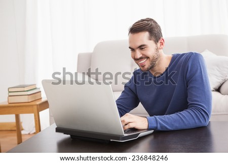 Smiling young man using his laptop at home in the living room