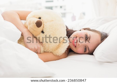 Pretty brunette under the duvet with teddy bear at home in the bedroom