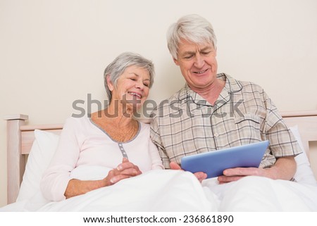 Senior couple relaxing in bed using tablet pc at home in bedroom