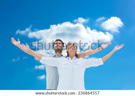 Cute couple standing with arms out against cloudy sky