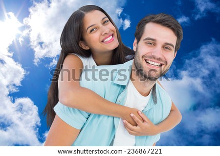 Happy casual man giving pretty girlfriend piggy back against bright blue sky with clouds