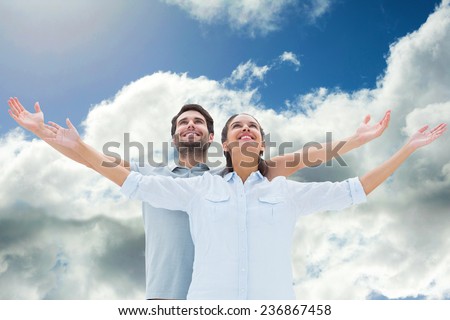 Cute couple standing with arms out against blue sky with clouds
