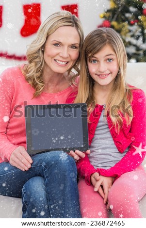 Festive mother and daughter showing tablet screen against snow falling