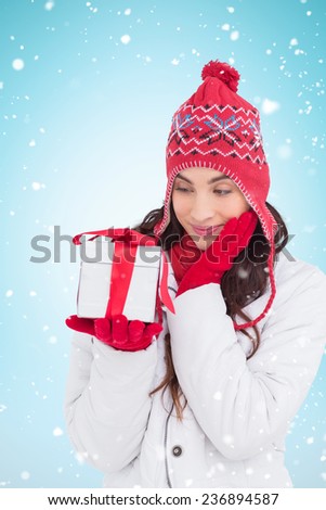 Content brunette in winter clothes holding gift against blue background with vignette