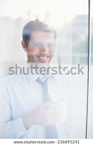 Smiling businessman holding mug looking out the window in his office