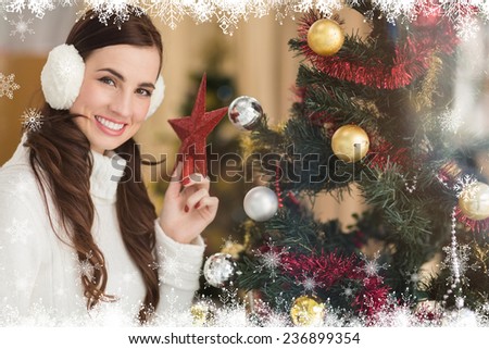 Smiling brunette holding star near a christmas tree against fir tree forest and snowflakes