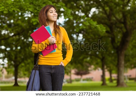 Smiling female college student with books looking away in the park