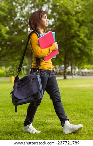 Side view of female college student with books walking in the park