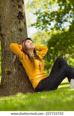 Side view of beautiful young woman sitting against tree in the park