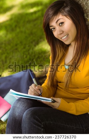 Portrait of female college student doing homework in the park