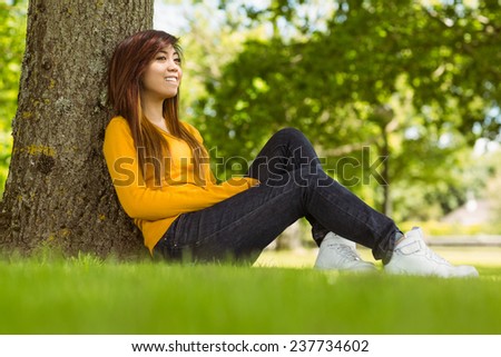 Side view of beautiful young woman sitting against tree in the park