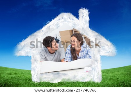 Couple lying on the floor and holding house plans against green field under blue sky