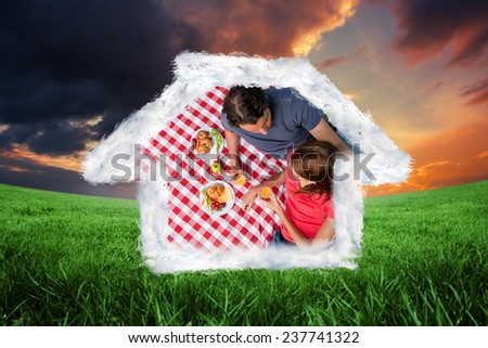 Elevated view of two friends lying on a blanket with a picnic against green field under orange sky