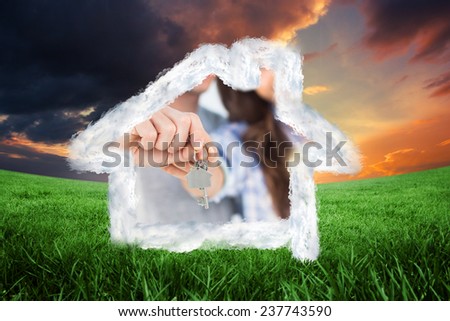 Man and wife presenting a key with a house keychain against green field under orange sky
