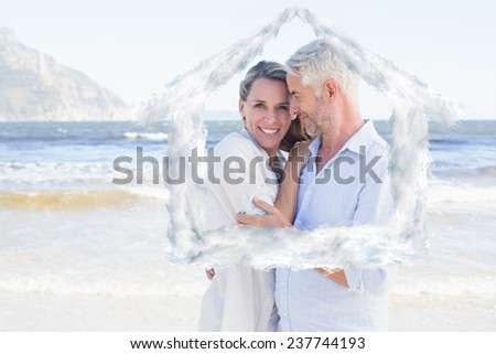 Happy couple hugging on the beach woman looking at camera against house outline in clouds