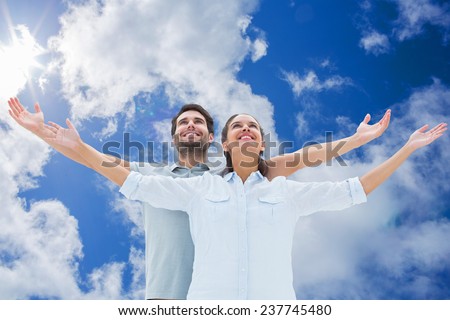 Cute couple standing with arms out against bright blue sky with clouds