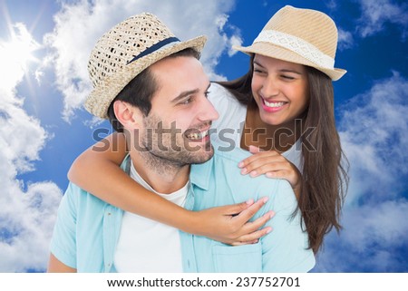 Happy casual man giving pretty girlfriend piggy back against bright blue sky with clouds