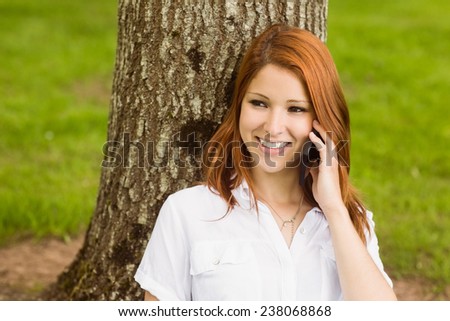 Pretty redhead smiling on the phone in park on a sunny day