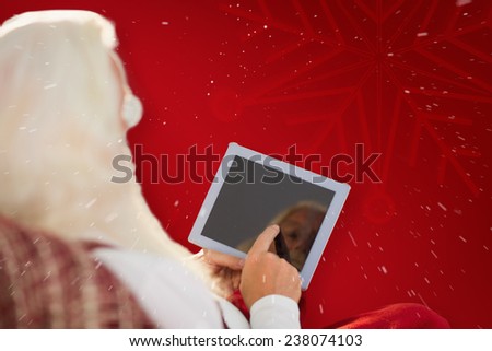 Rear view of santa using tablet on the armchair against red background