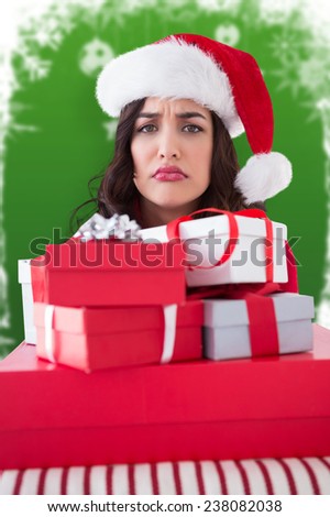 Confused brunette holding pile of gifts against fir trees with snow flakes