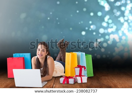 Brunette lying and using her laptop against shimmering light design over boards