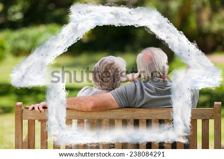 Couple sitting on the bench with their back to the camera against house outline in clouds