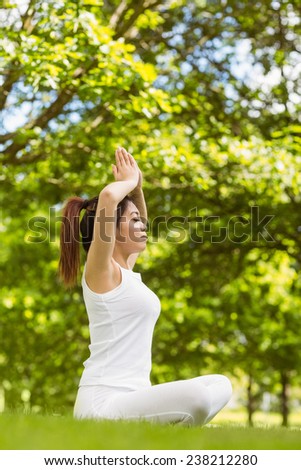 Full length of healthy and beautiful young woman sitting with joined hands over head at park