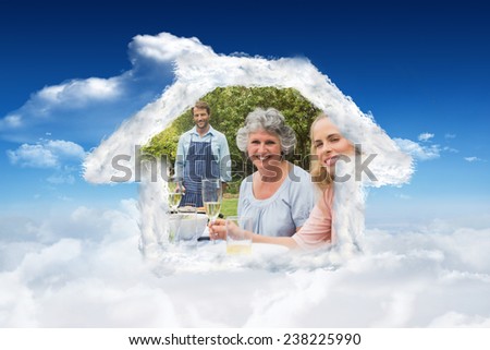 Happy extended family waiting for barbecue being cooked by father against bright blue sky with clouds