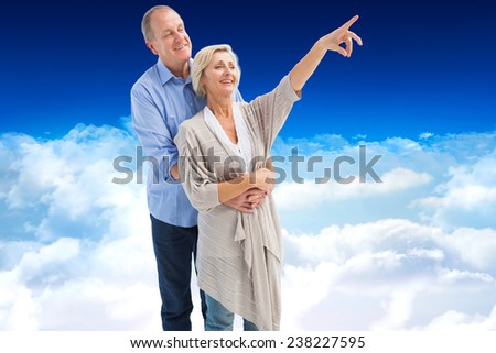 Happy mature couple embracing and looking against bright blue sky over clouds
