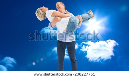 Mature man carrying his laughing partner against bright blue sky with clouds