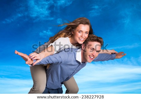 Smiling young man carrying woman against blue sky