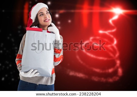 Thoughtful brunette holding shopping bag full of gifts against blurred christmas background