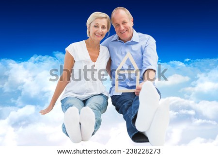 Happy mature couple holding a house shape against bright blue sky over clouds