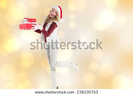 Smiling blonde in warm clothing holding pile of gifts against yellow abstract light spot design