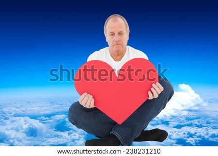 Upset man sitting holding heart shape against mountain peak through the clouds